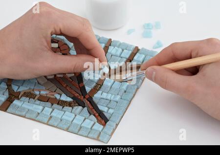 Coller les carreaux de mosaïque en sens inverse sur le papier brun à l'aide de colle PVA lavable, appliqué avec une petite brosse, gros plan Banque D'Images