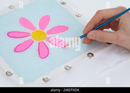 Femme utilisant un pinceau fin pour peindre dans la couleur pétale de fleur sur le cadre batik, gros plan Banque D'Images