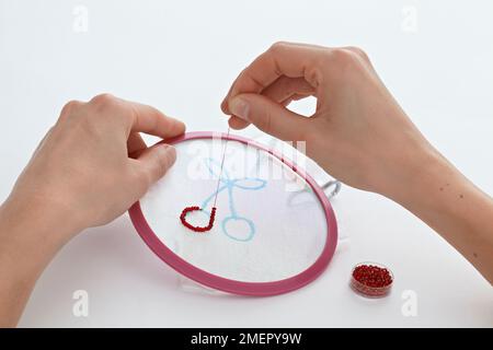 Femme couture de perles rouges sur le modèle de cerise sur la boucle de broderie, gros plan Banque D'Images