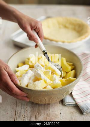 Mélanger la farine de maïs et le sucre avec des tranches de pomme dans un bol à mélanger (faire de la tarte aux pommes) Banque D'Images