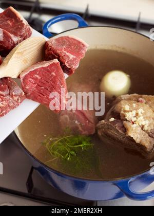 Ingrédients (morceaux de steak) ajoutés au pot-au-feu Banque D'Images