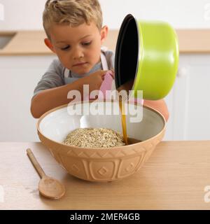 Garçon versant du sirop dans un bol d'avoine porridge, 4 ans Banque D'Images