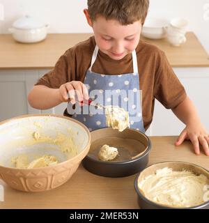 Garçon mettant le mélange éponge dans des moules à gâteau, 8 ans Banque D'Images