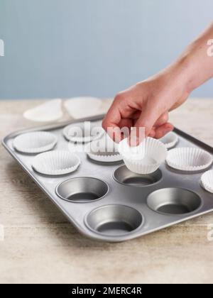 Doublure du moule à pain avec des étuis en papier pour préparer des petits gâteaux Banque D'Images