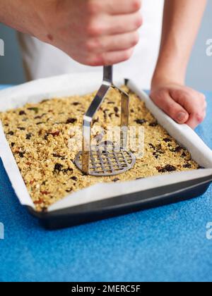 À l'aide d'un presse-purée, enfoncer fermement le mélange de barres de muesli dans un moule à pâtisserie, en faisant des barres de muesli (barres de céréales et de fruits) Banque D'Images