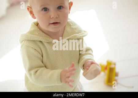 Bébé fille portant un sweat à capuche tricoté jouant avec le jouet sur le sol, 17 mois Banque D'Images