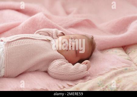 Bébé fille allongé portant un gilet tricoté rose, 6 semaines Banque D'Images