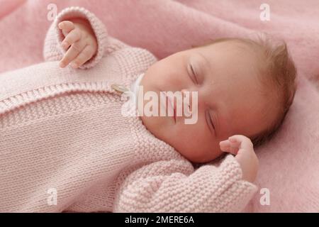 Bébé fille allongé portant un gilet tricoté rose, 6 semaines Banque D'Images