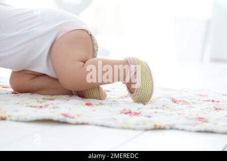 Bébé fille rampant portant des chaussons tricotés, 9 mois Banque D'Images