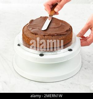 Gâteau de Savoie au chocolat glacé avec glaçage au ganache au chocolat à l'aide d'une spatule Banque D'Images