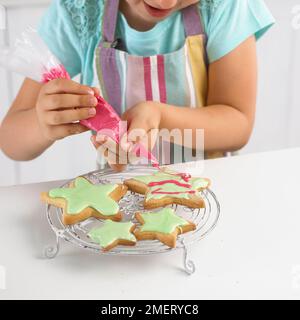 Girl decorating cookies en forme d'étoile avec du glaçage Banque D'Images