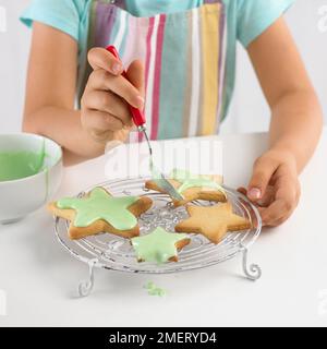 Girl decorating cookies en forme d'étoile avec du glaçage Banque D'Images