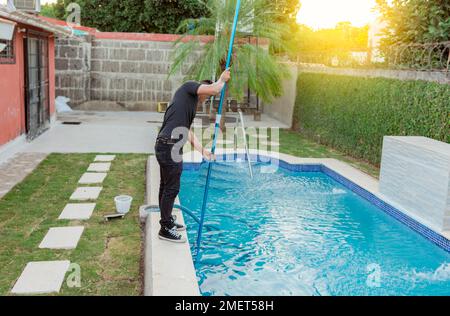 Homme nettoyant et entretenant les piscines avec un tuyau d'aspiration. Un jeune homme qui nettoie une piscine avec un tuyau d'aspiration, un agent d'entretien qui nettoie Banque D'Images