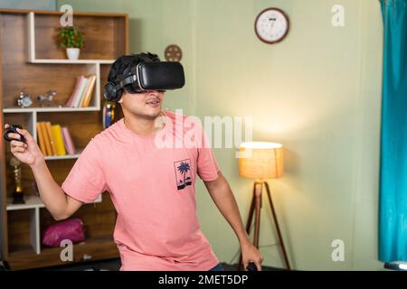 Vue latérale de Jeune homme avec VR ou réalité virtuelle gogles jouant à un jeu vidéo avec joystick sur métaverse à la maison - l'appart de la technologie, de la détente et Banque D'Images