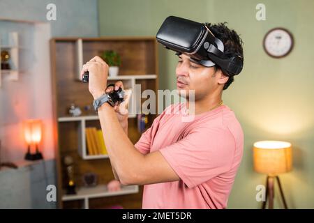 Un jeune homme doux et fatigué avec des lunettes VR ou de réalité virtuelle vérifiant les calories brûlées sur la montre intelligente après l'entraînement sur VR à la maison - concept de détente Banque D'Images