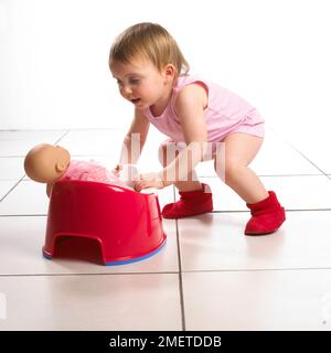 Fille crouching tout en mettant la poupée en pot rouge, 19 mois Banque D'Images