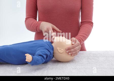 Les contrôles médicaux de premiers soins et le traitement de l'enfant inconscient, à l'aide de mannequin, s'assurer que les voies respiratoires sont encore ouverts en gardant une main sur le front et au doigt de l'autre main sous le bout du menton de l'enfant, donnant le CFCP Banque D'Images
