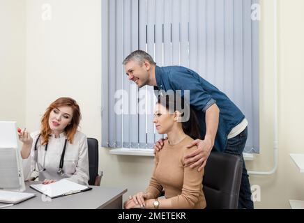 Un couple heureux planifiant une grossesse et rendant visite à un médecin à la clinique. Une femme médecin consulte un couple marié dans un bureau médical. Banque D'Images