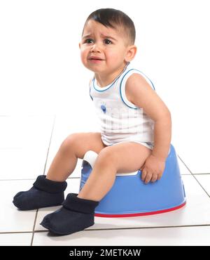 Garçon portant un gilet et des chaussons assis sur un pot bleu, 15 mois Banque D'Images