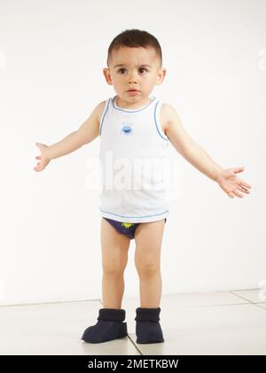 Garçon portant un gilet, un pantalon et des pantoufles avec les bras étirés, 15 mois Banque D'Images