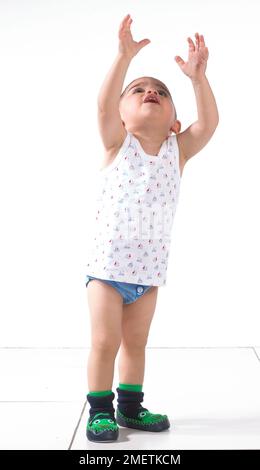 Garçon portant un gilet, un pantalon et des pantoufles avec les bras dans les airs, 15 mois Banque D'Images