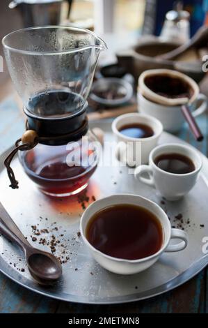 Caffe Touba, vidange du café par un chiffon dans une verseuse en verre, trois tasses de café sur un plateau Banque D'Images