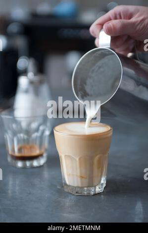 Dorez, versez du lait et de la crème cuits à la vapeur sur une dose d'espresso Banque D'Images