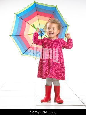 Petite fille (2 ans) portant des bottes wellington et holding umbrella Banque D'Images