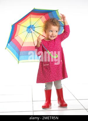 Petite fille (2 ans) portant des bottes wellington et holding umbrella Banque D'Images