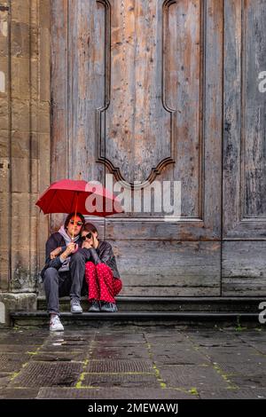 Jeune couple assis sur le pas de la porte sous un parapluie rouge à Florence, en Italie. Banque D'Images