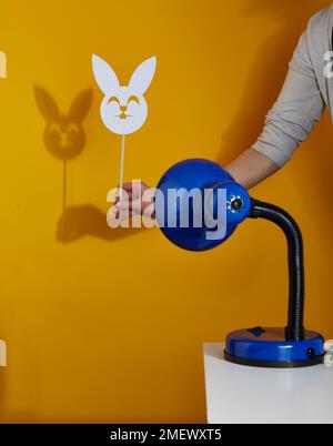 Lampe de table bleue projetant l'ombre d'un masque de lapin sur un fond jaune Banque D'Images