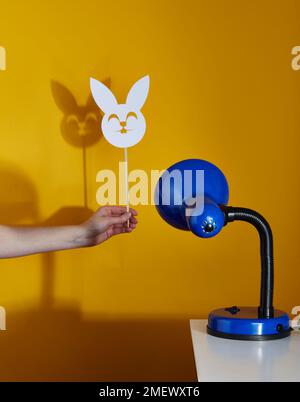 Lampe de table bleue projetant l'ombre d'un masque de lapin sur un fond jaune Banque D'Images