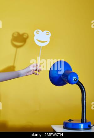 Lampe de table bleu jette une ombre d'un masque de grenouille sur un fond jaune Banque D'Images