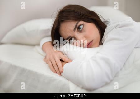 Une jeune femme ennuyeuse, couchée dans un lit seul à la maison Banque D'Images
