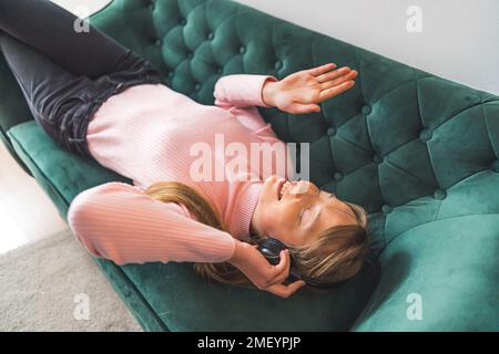 Femme souriante, les yeux fermés, écoutant de la musique dans un casque sur un canapé. Photo de haute qualité Banque D'Images