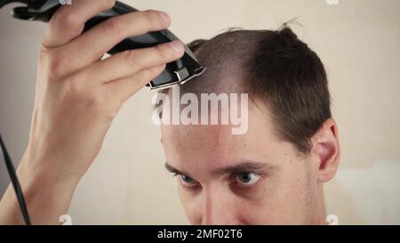 À la maison, un homme rasse sa tache chauve devant un miroir. problème de perte de cheveux Banque D'Images