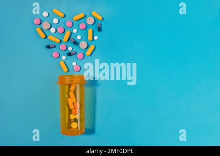 Pilules, comprimés et capsules disposés en forme de coeur, bouteille orange sur fond bleu. Concept de médicament Banque D'Images