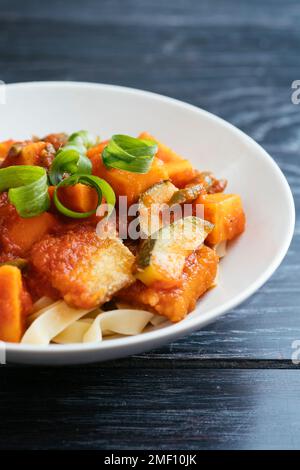 Haricots verts, patates douces et courgettes dans une sauce douce et épicée avec tofu frit, servi sur des pâtes. Banque D'Images