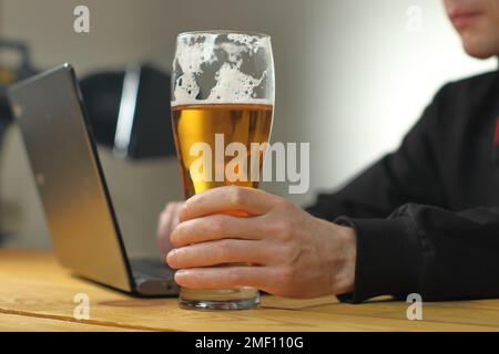 personne tenant une tasse à bière près d'un ordinateur portable sur fond gris Banque D'Images