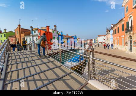 Femme appuyée sur un pont métallique sur le canal dans l'île colorée de Burano dans la lagune vénitienne, Vénétie, Italie. Banque D'Images