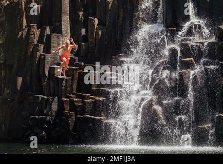 Homme d'âge moyen sautant dans un lac en cascade. Des jets d'eau tombent sur des cascades de pierre volcanique noire. Chutes d'eau de Rochester - populaire sp Banque D'Images
