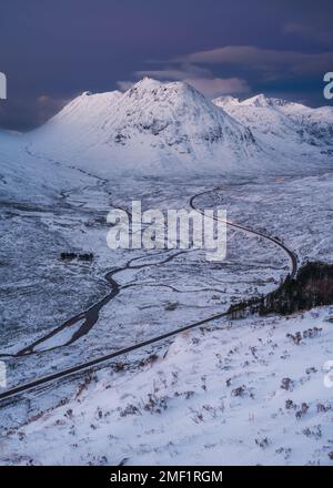 Longue route sinueuse menant à travers la vallée enneigée de Glencoe, Royaume-Uni. Banque D'Images