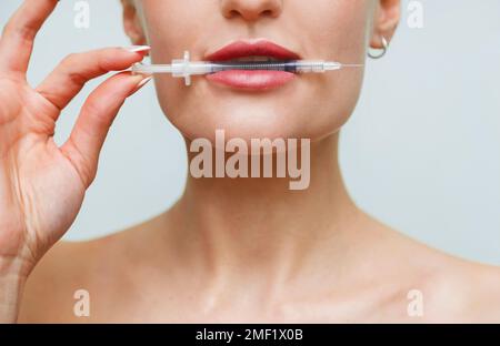 Gros plan visage jeune femme tient la seringue dans la bouche. Injection de collagène acide hyaluronique pour les lèvres Banque D'Images