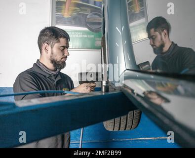 Vue latérale du maître mâle à l'aide d'un tournevis électrique lors de la fixation de la roue de l'automobile soulevée dans un atelier professionnel Banque D'Images