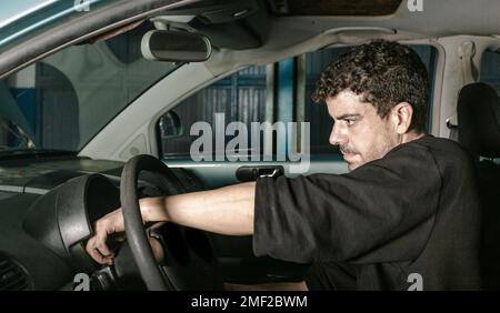 Vue latérale d'un technicien homme assis dans une voiture et vérification des informations de dépannage lors de travaux dans un atelier d'entretien automobile Banque D'Images