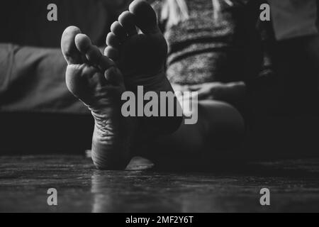 une fille est assise sur un sol en bois sale, un canapé rouge est versé dans les chambres à la maison, au repos, au repos à la maison, les pieds sur le sol pieds nus Banque D'Images