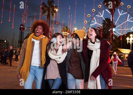 Groupe d'amis qui marchent dans le parc d'attractions la nuit avec leurs bras l'un autour de l'autre. Banque D'Images