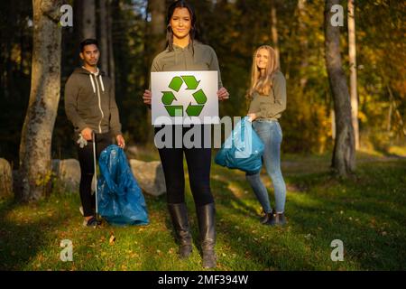 Femme volontaire confiante tenant l'étiquette du symbole de recyclage devant l'équipe Banque D'Images