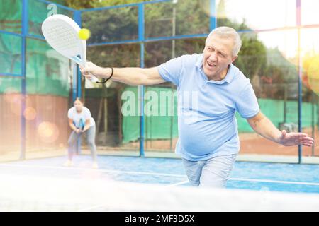 Homme âgé jouant au paddleball sur un terrain extérieur Banque D'Images