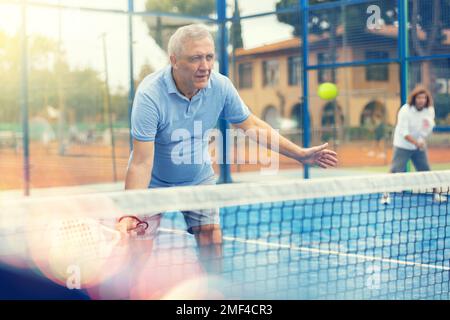 Ederly homme jouant au padel tennis sur un terrain ouvert Banque D'Images